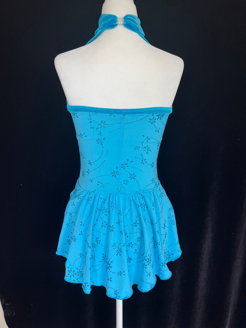 May include: A light blue figure skating dress with a halter neckline and a floral pattern. The dress has a ruffled skirt and a velvet trim.
