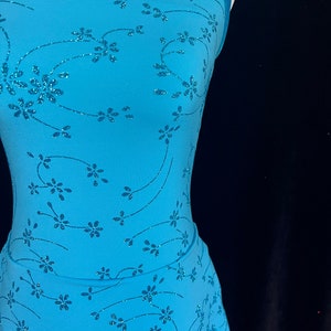 May include: A light blue figure skating dress with a floral pattern and glitter accents. The dress has a halter neckline and a skirt with a ruffled hem.