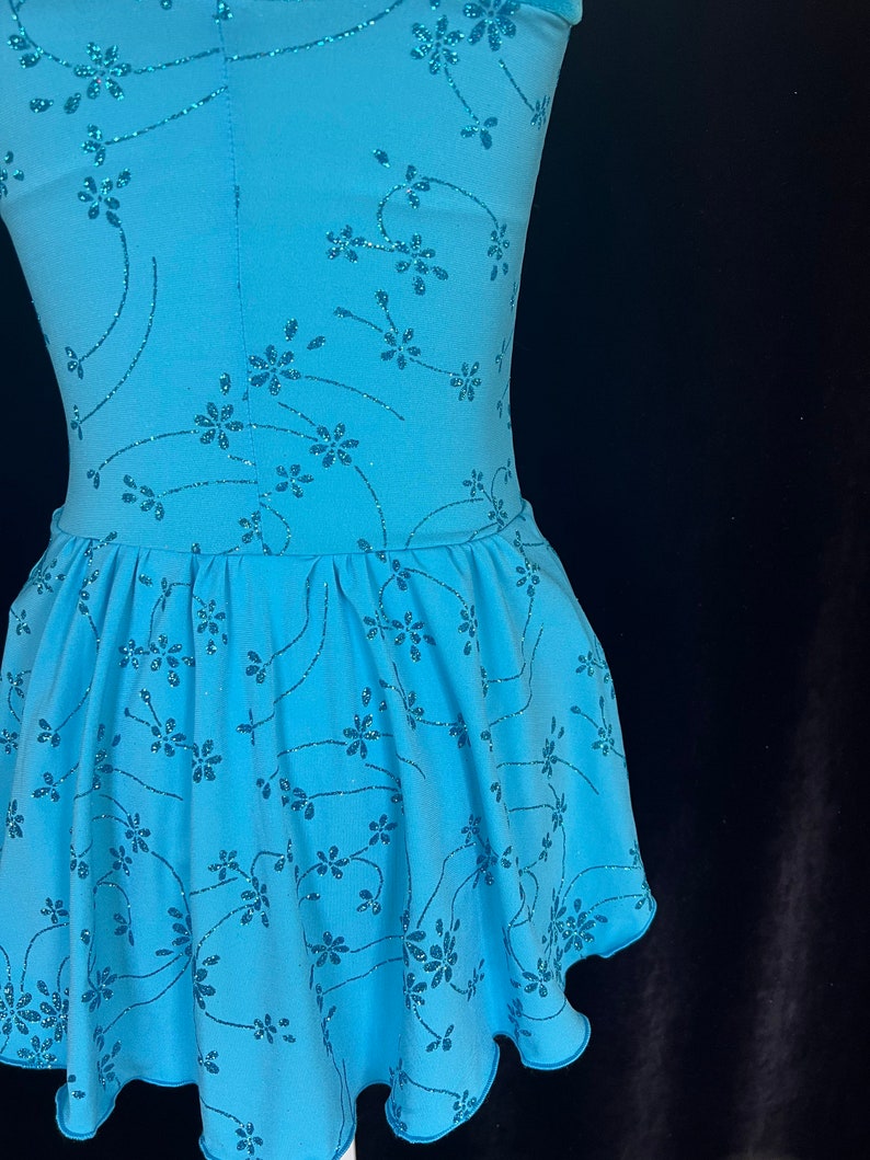May include: A light blue dance dress with a floral pattern and glitter accents. The dress has a fitted bodice and a flared skirt.