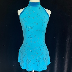 May include: A turquoise blue sleeveless leotard with a floral pattern. The leotard has a high neckline and a fitted bodice. The skirt is a flared, layered design.