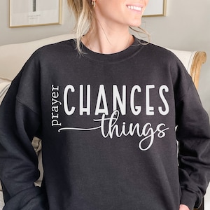 Peut inclure: Sweat-shirt noir avec un texte blanc qui dit "la prière change les choses".