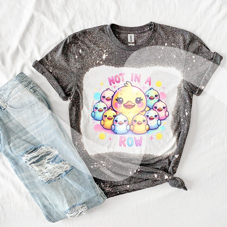 Puede incluir: Una camiseta negra y blanca blanqueada con un gr&aacute;fico de patitos amarillos con detalles rosas y azules. El texto "NOT IN A ROW" est&aacute; impreso debajo de los patitos.