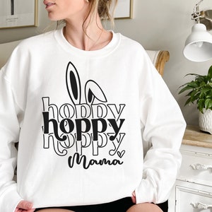 May include: White sweatshirt with a black graphic design that says "hoppy hoppy mama" with bunny ears above the text.