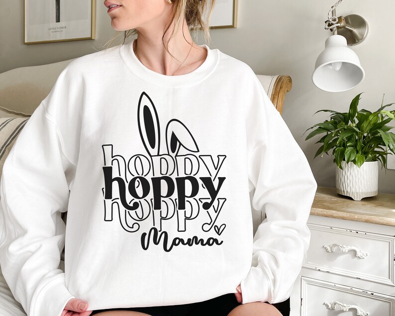 May include: White sweatshirt with a black graphic design that says "hoppy hoppy mama" with bunny ears above the text.