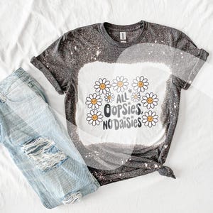 May include: A black and white bleached t-shirt with a graphic design of daisies and the text "All * Oops* No Daisies".