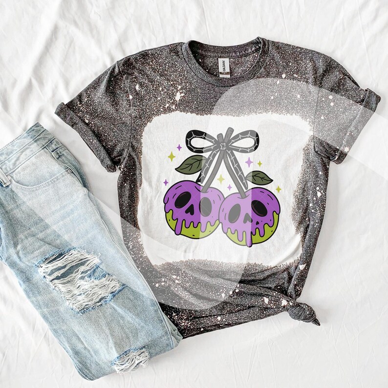 May include: A dark gray t-shirt with a white bleached design featuring a pair of purple cherries with skull faces and green accents. The shirt is paired with light blue ripped jeans.