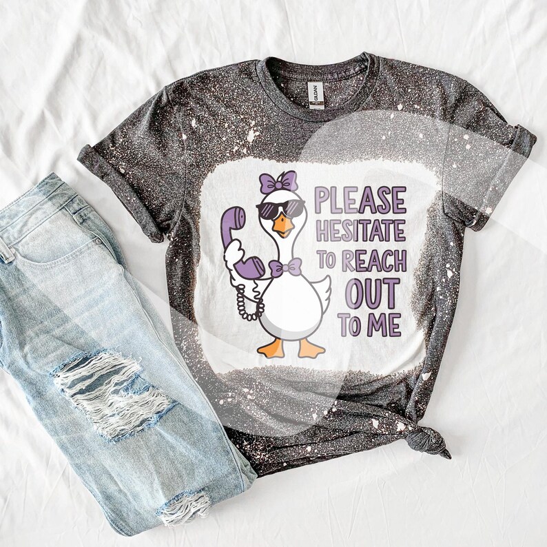 May include: A black and white bleached t-shirt with a cartoon goose wearing sunglasses and holding a purple phone. The text on the shirt reads "Please Hesitate To Reach Out To Me".