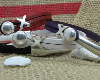 May include: Three leather bracelets with silver star charms and silver clasps. The bracelets are layered on top of each other. The top bracelet is red, the middle bracelet is white, and the bottom bracelet is black.