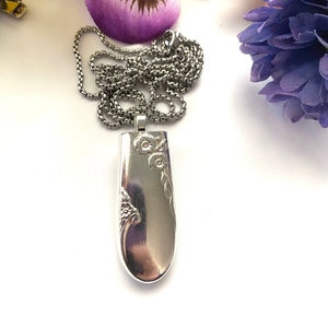 May include: A silver necklace with a pendant shaped like a spoon with floral designs. The pendant is attached to a silver chain.