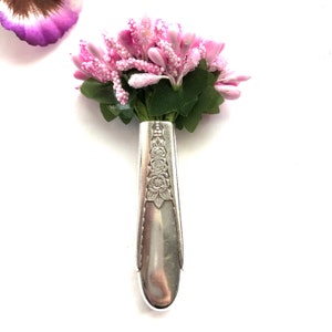 Puede incluir: Un ramo de flores rosas en un jarrón plateado hecho con un mango de cubiertos reutilizado.