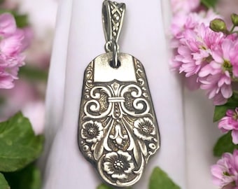 Puede incluir: Un colgante de plata con un diseño floral. El colgante está hecho de una cuchara vintage reutilizada y tiene un patrón floral detallado.