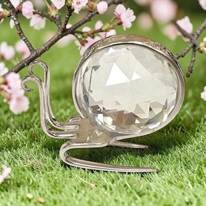 May include: A decorative snail figurine crafted from a silver-toned metal fork, featuring a large, clear, multifaceted spherical crystal as the shell. The metal handle is curved to form the body and antennae, while the tines form the base.