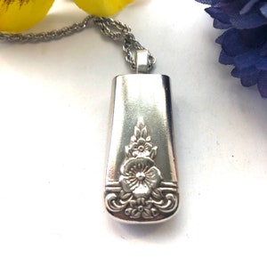 May include: A silver necklace with a pendant made from a vintage silverware handle. The handle has a floral design with a large flower in the center.