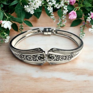 May include: A silver bracelet made from a vintage spoon with a floral design. The bracelet is open and has a magnetic clasp.