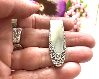May include: A silver spoon with a floral design. The spoon is oval shaped and has a smooth, polished surface. The floral design is intricate and detailed, with small flowers and leaves.