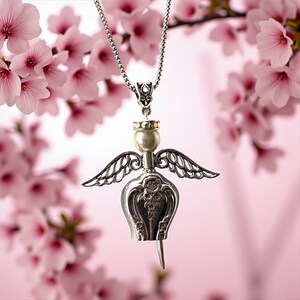 May include: A silver-toned angel pendant with a pearl head and detailed wings hangs from a delicate chain. The pendant is set against a soft pink background with blurred pink blossoms, creating a delicate and ethereal aesthetic.