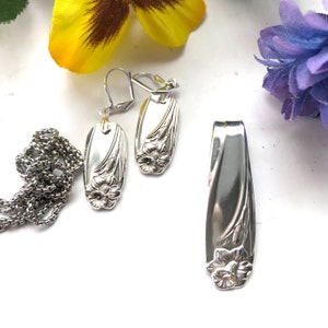 May include: A silver necklace, earrings, and pendant set featuring a floral design. The jewellery is made from repurposed silverware and has a vintage aesthetic.