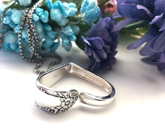 Puede incluir: Un collar de plata con un colgante en forma de corazón hecho de una cuchara vintage con detalles florales. El collar está en una cadena de plata.