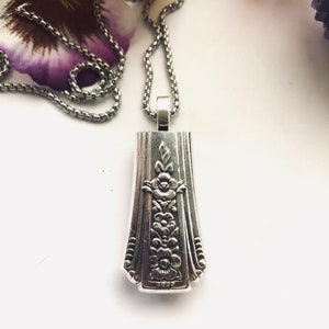 May include: A silver necklace with a pendant made from a vintage silverware piece. The pendant features a floral design with a raised pattern.