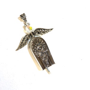 May include: A handcrafted silver angel pendant. The angel features ornate filigree wings, a clear crystal bead head, and a spoon-shaped body with floral detailing. The pendant is designed to be worn as jewelry.
