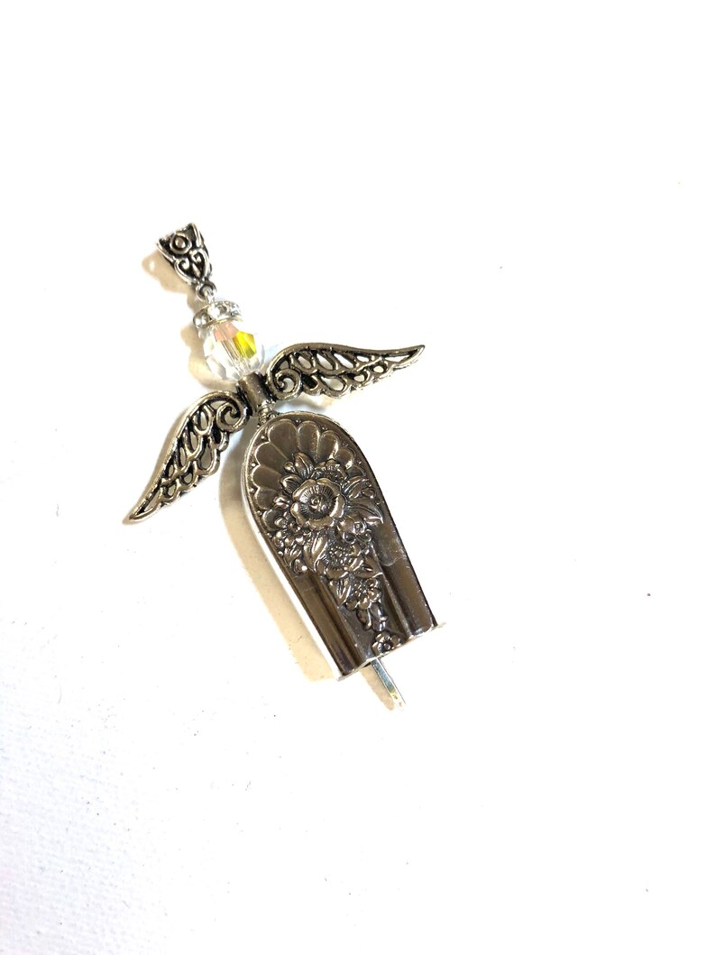 May include: A handcrafted silver angel pendant. The angel features ornate filigree wings, a clear crystal bead head, and a spoon-shaped body with floral detailing. The pendant is designed to be worn as jewelry.