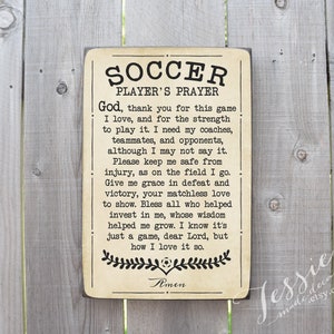 May include: A brown wooden sign with a beige background and black text. The sign reads "Soccer Player's Prayer" and includes a prayer for a soccer player. The sign is decorated with a soccer ball and a floral design.