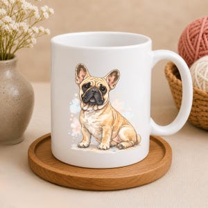 May include: White ceramic mug featuring a watercolor illustration of a tan and black French Bulldog. The dog is sitting with its ears perked up. The mug sits on a round wooden coaster.