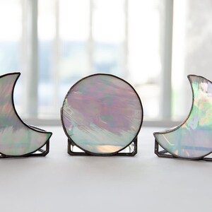 May include: Three iridescent glass moon-shaped candle holders. The candle holders are made of stained glass and have a silver finish.