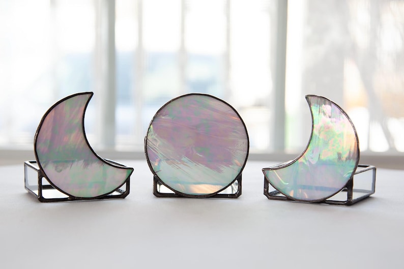 May include: Three iridescent glass moon-shaped candle holders. The candle holders are made of stained glass and have a silver finish.