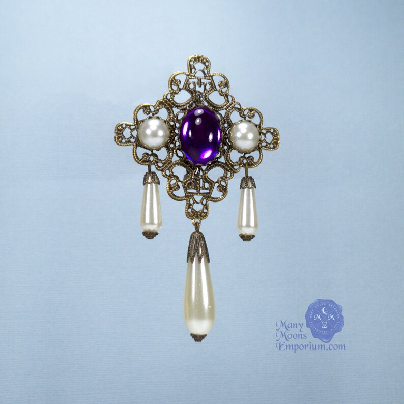 May include: A gold filigree brooch with a purple gemstone and three pearl drops.