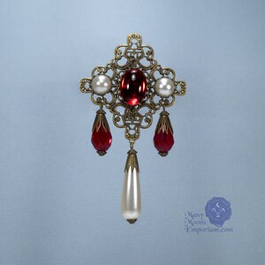 May include: A gold filigree pendant with a red glass center stone and white pearl accents. The pendant has three dangling red glass drops and a single white pearl drop.