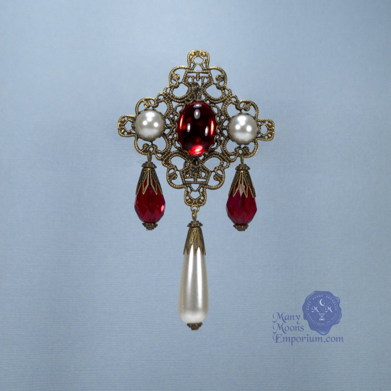 May include: A gold filigree pendant with a red glass center stone and white pearl accents. The pendant has three dangling red glass drops and a single white pearl drop.
