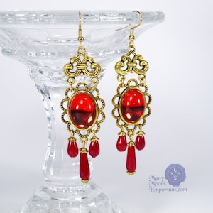 May include: Gold dangle earrings with red glass stones and gold filigree details.