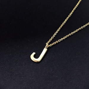 May include: A gold chain necklace with a small gold letter J pendant. The necklace is displayed on a black box.