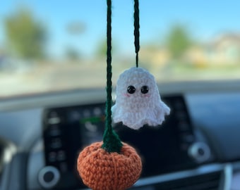 May include: A white crocheted ghost and an orange crocheted pumpkin hanging from a rearview mirror in a car.