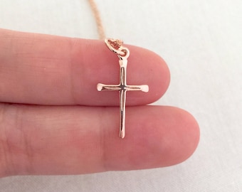 Könnte beinhalten: Eine zarte Halskette mit einem Kreuzanhänger aus Roségold. Das Kreuz ist schlicht und elegant und hat eine leicht strukturierte Oberfläche.