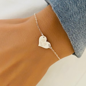 May include: A silver chain bracelet with a heart-shaped charm. The charm has a paw print engraved on it.