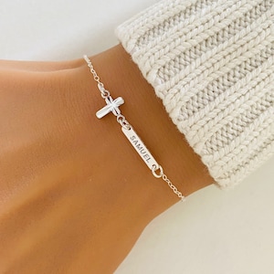 May include: Silver bracelet featuring a cross charm and a personalised nameplate inscribed with "SAMUEL".