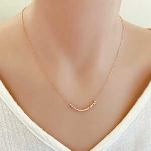 May include: A delicate gold chain necklace with a small row of gold beads and bars hanging from it.