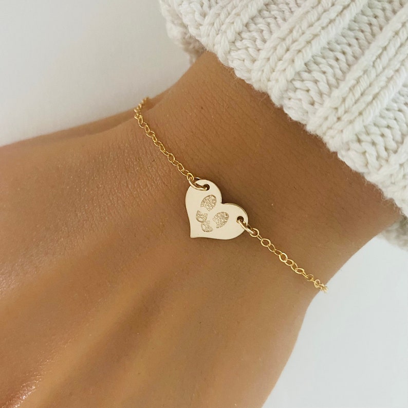 May include: A gold chain bracelet with a heart-shaped charm featuring a paw print design.