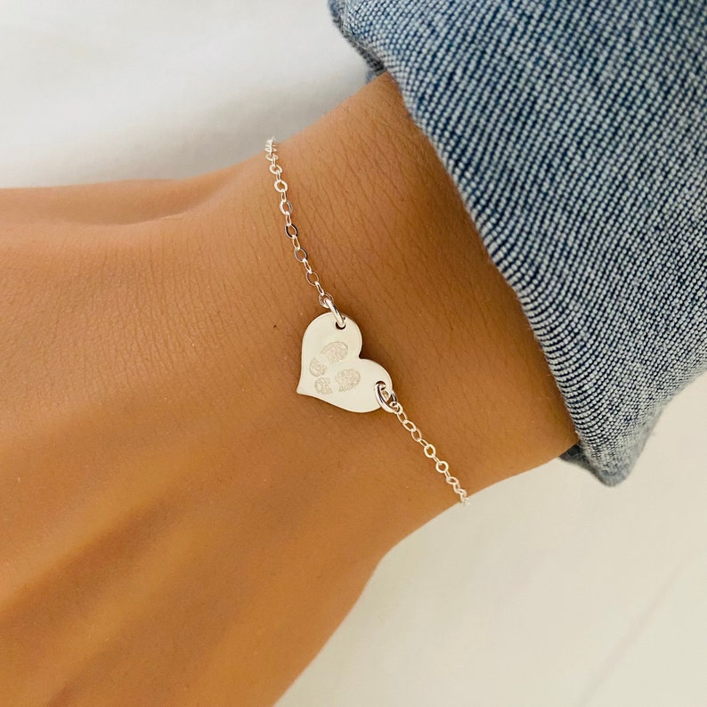 May include: A silver chain bracelet with a heart-shaped charm. The charm has a paw print engraved on it.