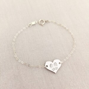 May include: A silver chain bracelet with a heart-shaped charm featuring paw prints.