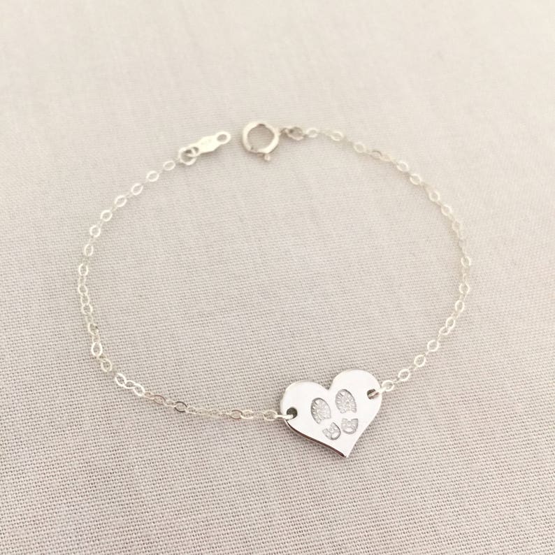 May include: A silver chain bracelet with a heart-shaped charm featuring paw prints.