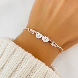 Può includere: Braccialetto d'argento con due ciondoli a forma di cuore incisi con le lettere "A" e "L" e due ciondoli ad ali d'angelo.