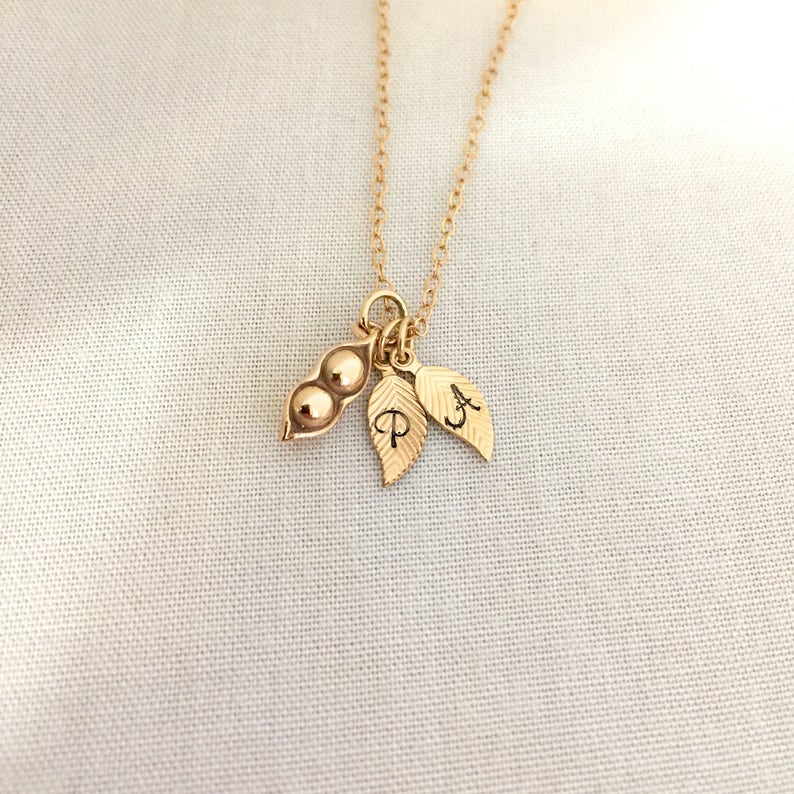 May include: Gold necklace with a pea pod charm and two leaf charms with the letters "P" and "A" engraved on them.