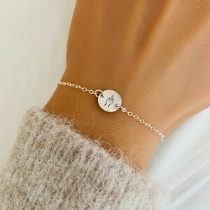 Puede incluir: Un brazalete de cadena de plata con un dije redondo que muestra un dedo medio.
