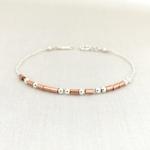 May include: A delicate silver chain bracelet with alternating silver beads and rose gold colored bars.