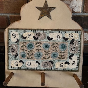 May include: A wooden wall-mounted rack with a star and a hand-stitched rug featuring a floral pattern and sheep. The rack has three hooks for hanging items.