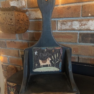 May include: A dark blue wooden dustpan with a long handle and a decorative square insert. The insert features a horse, stars, and text. The dustpan is displayed against a brick wall.