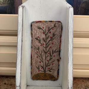May include: A white, distressed wooden wall shelf with a decorative, rectangular rug insert. The rug features a tree design with red berries on a brown background. The shelf has a curved top and a rustic, farmhouse aesthetic.